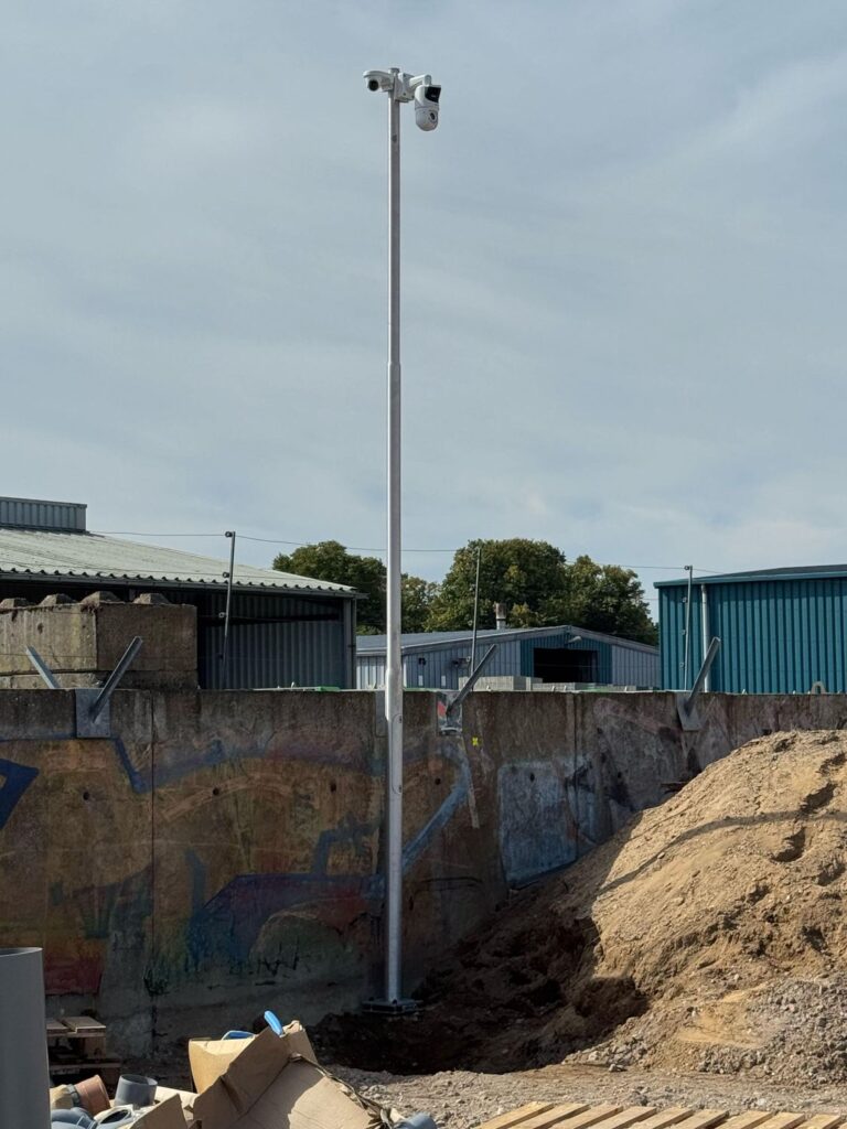 Mast met twee camera's op een bedrijventerrein met keerwanden en loodsen
