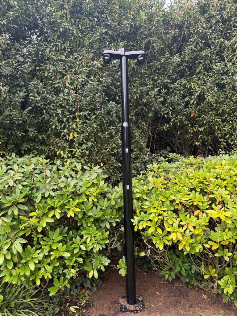 Zwarte camerapaal met twee camera's tussen de beplanting in een tuin