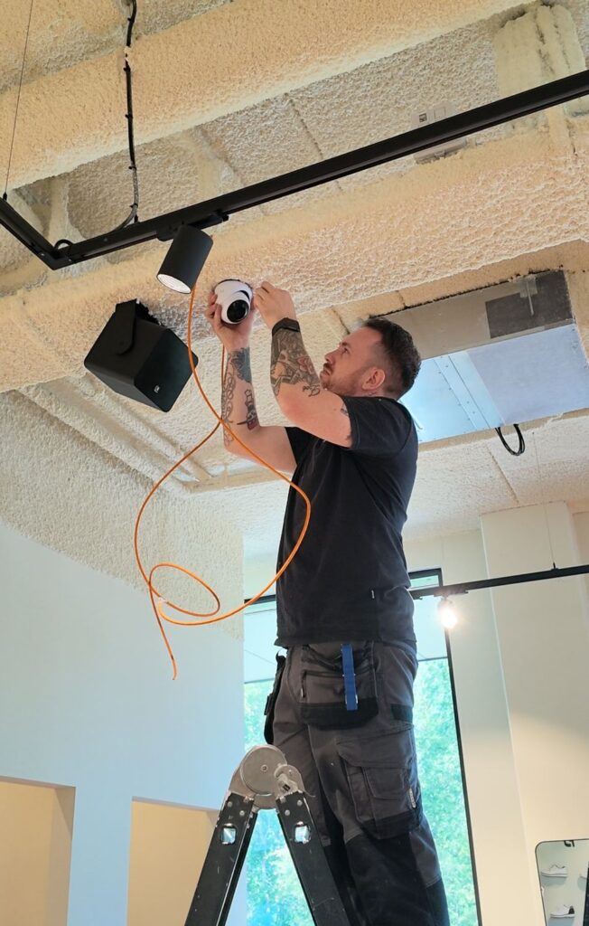 Monteur op een ladder plaatst een camera aan een akoestisch plafond