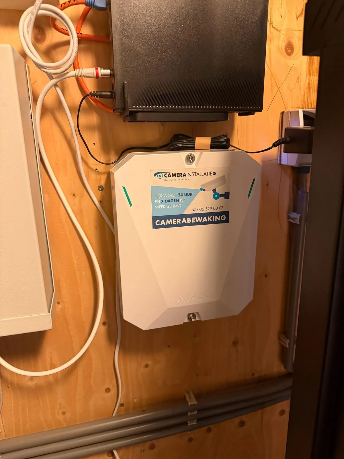 Alarmcentrale met sticker in een meterkast, de recorder erboven en de kabels in buizen eronder