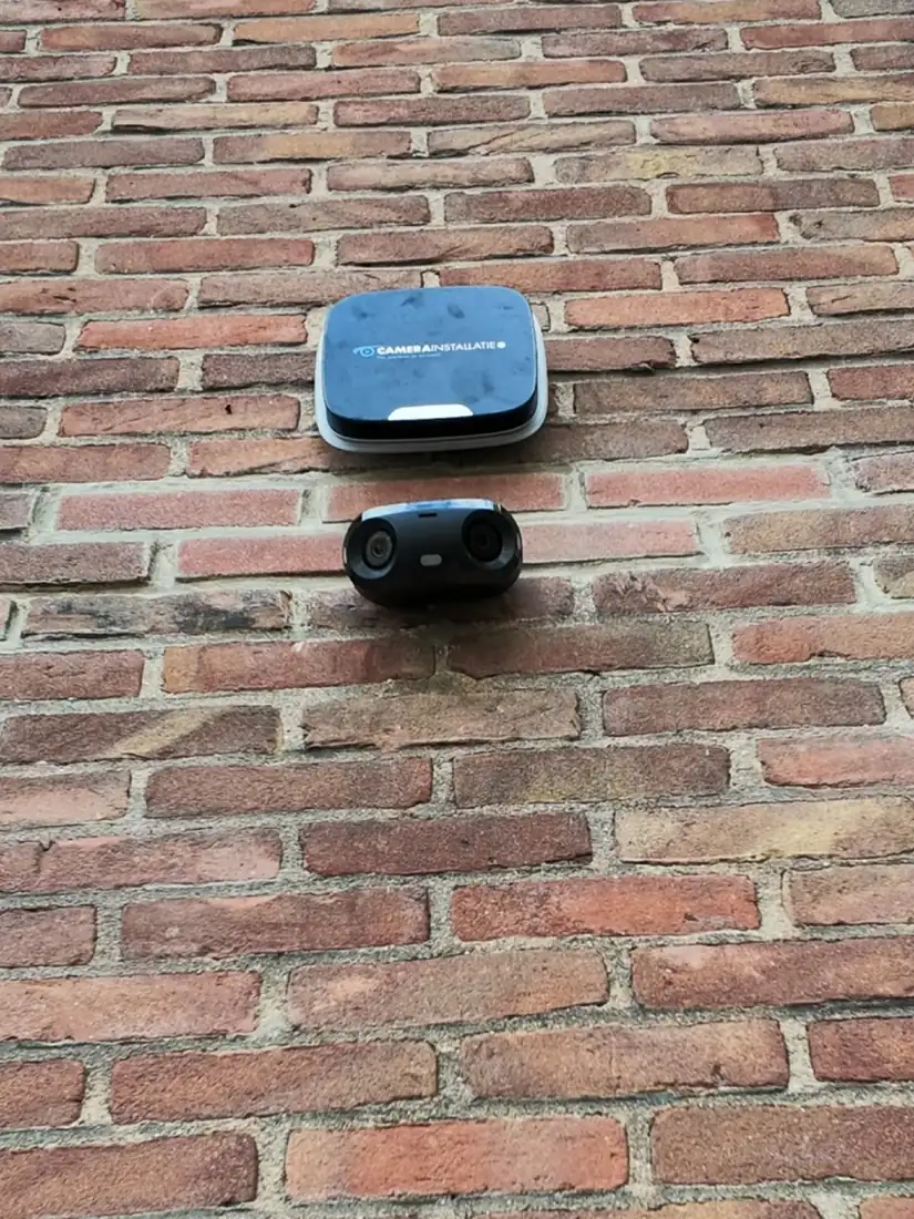 Buitensirene met daaronder een camera met twee lenzen op een bakstenen gevel