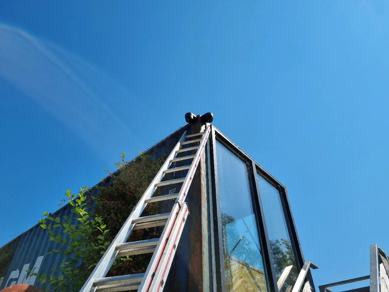 Ladder tegen een containergebouw met veel glas, met twee camera's op de hoek van het dak