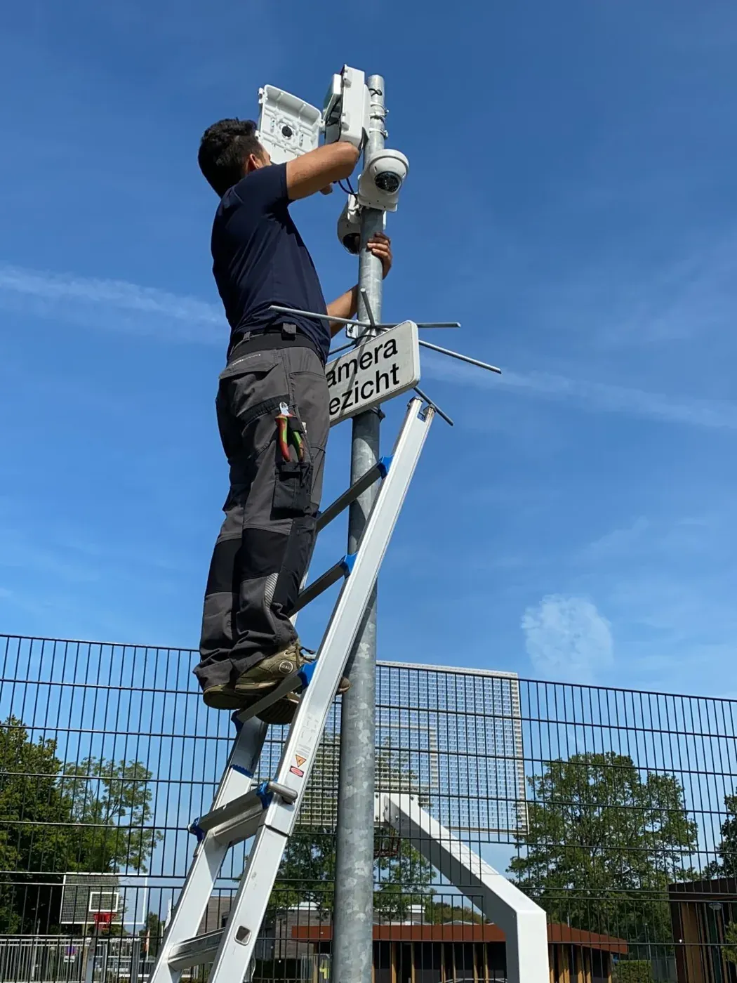 Monteur op een ladder hangt een camera aan de paal langs het hekwerk