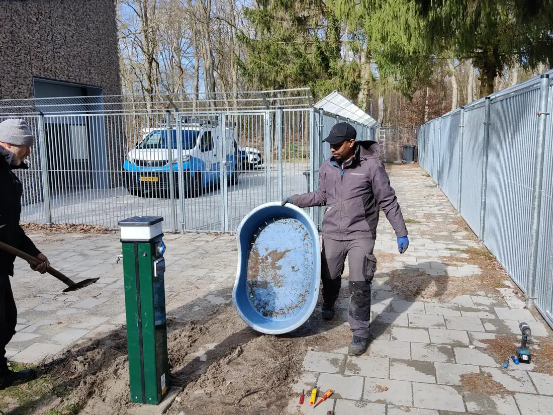 Twee monteurs plaatsen een toegangspaal bij een hekwerk